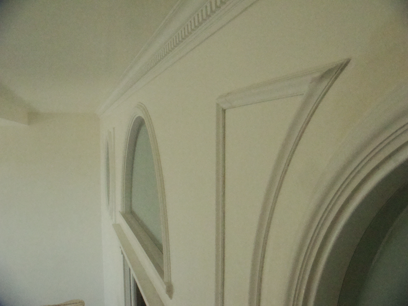 Primo piano di una parete interna bianca con modanature decorative e pannelli a muro arcuati e incassati.