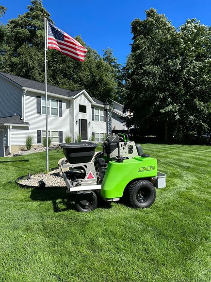 A green lawn mower is parked in the grass in front of a house.