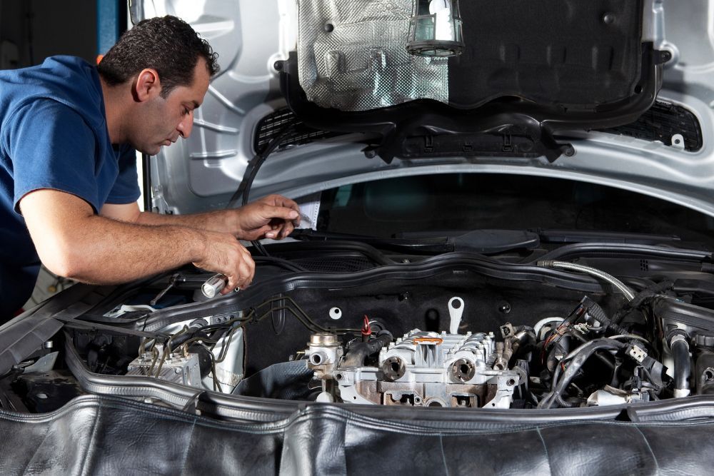 Mechanic working on a car engine with the hood open, indoors. | Elite Autocare of Princeton