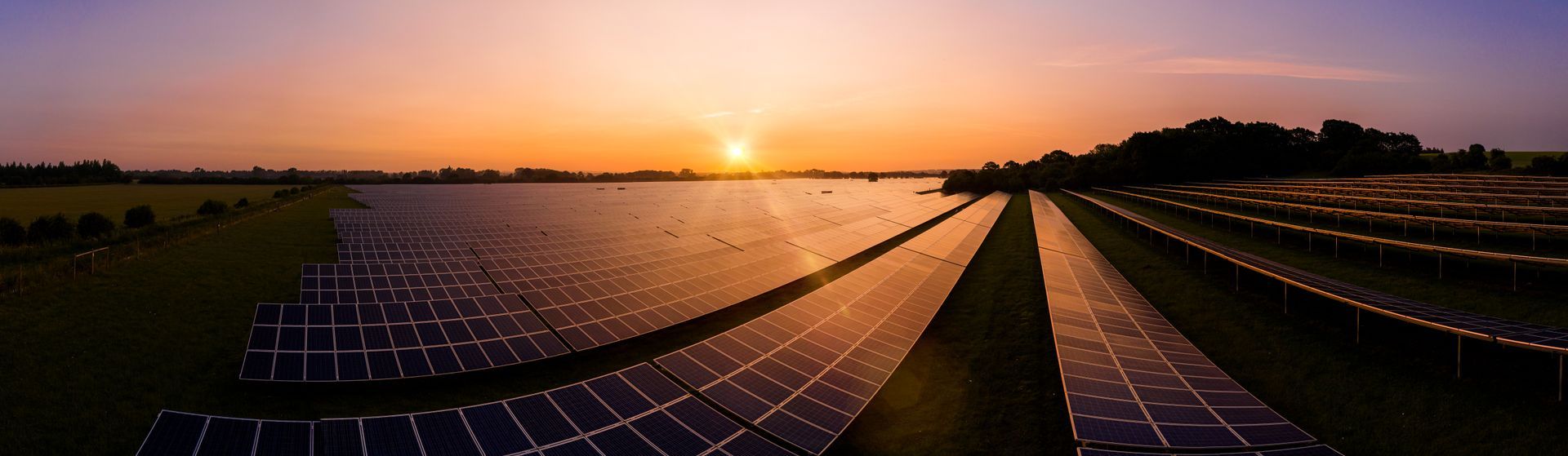 A row of solar panels sitting next to a body of water at sunset.