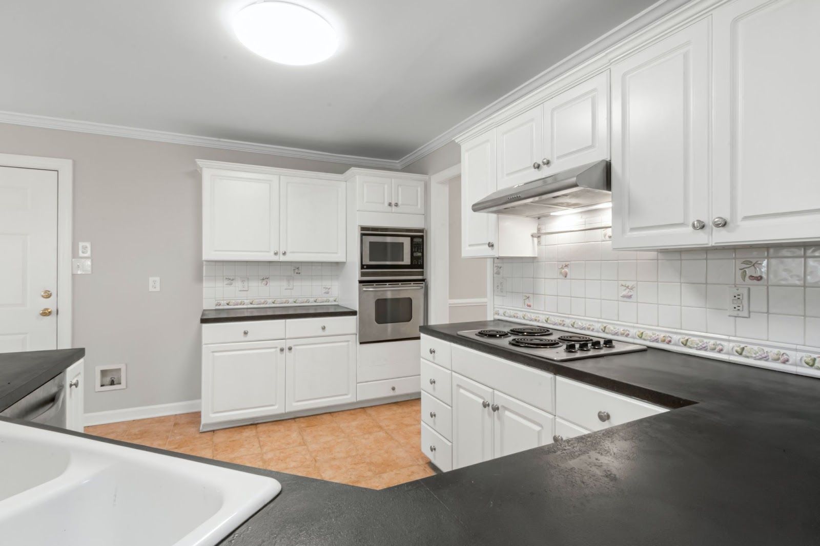 White kitchen with black countertops, stainless steel appliances, and white cabinets.