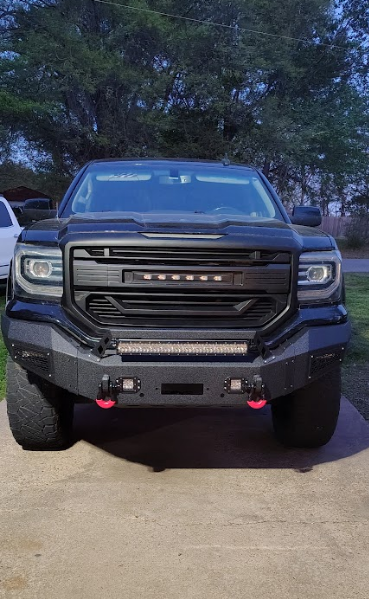 A black truck is parked in a driveway with trees in the background.