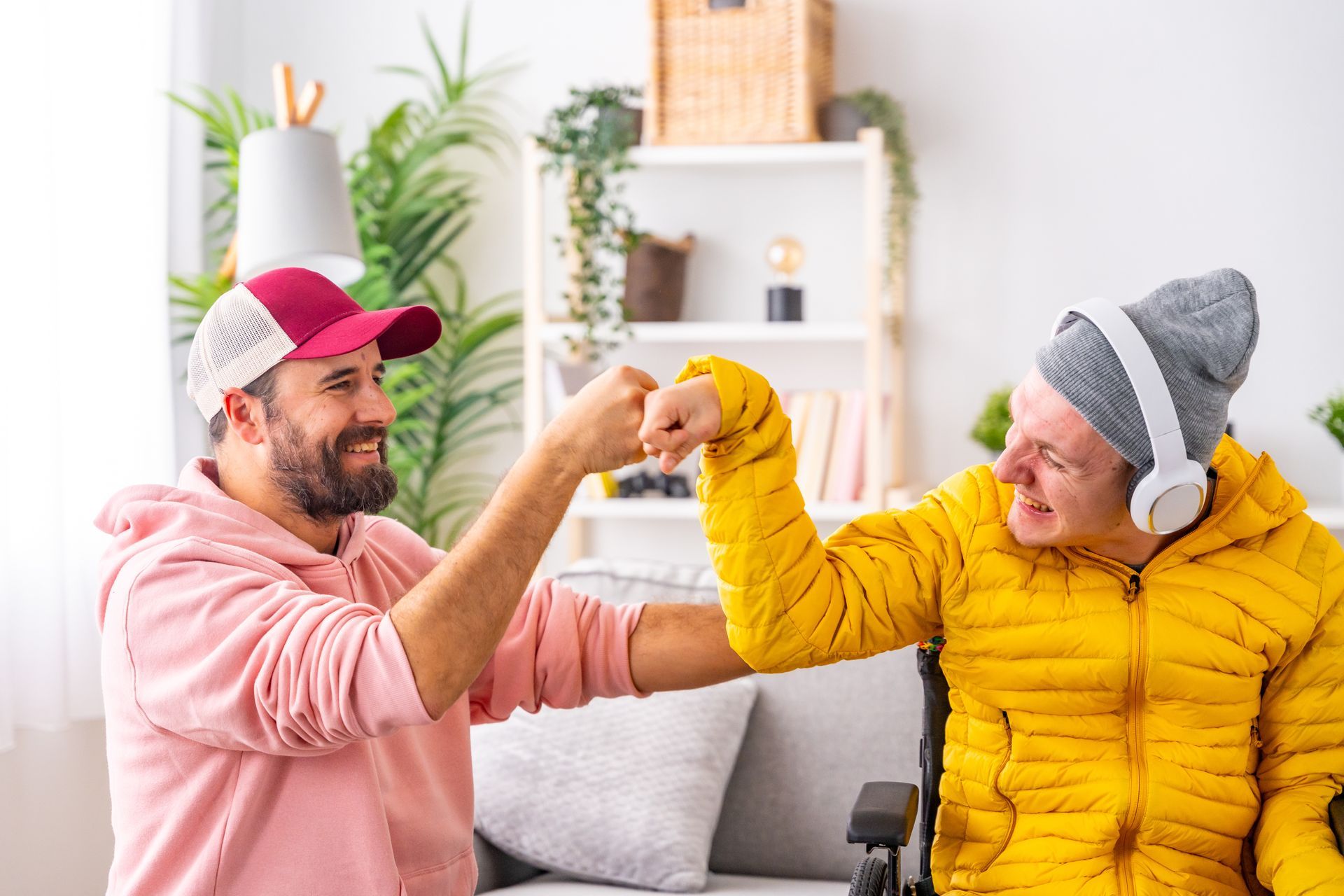 Two people in bright sweaters fist-bump while sitting on a couch in a cozy living room.