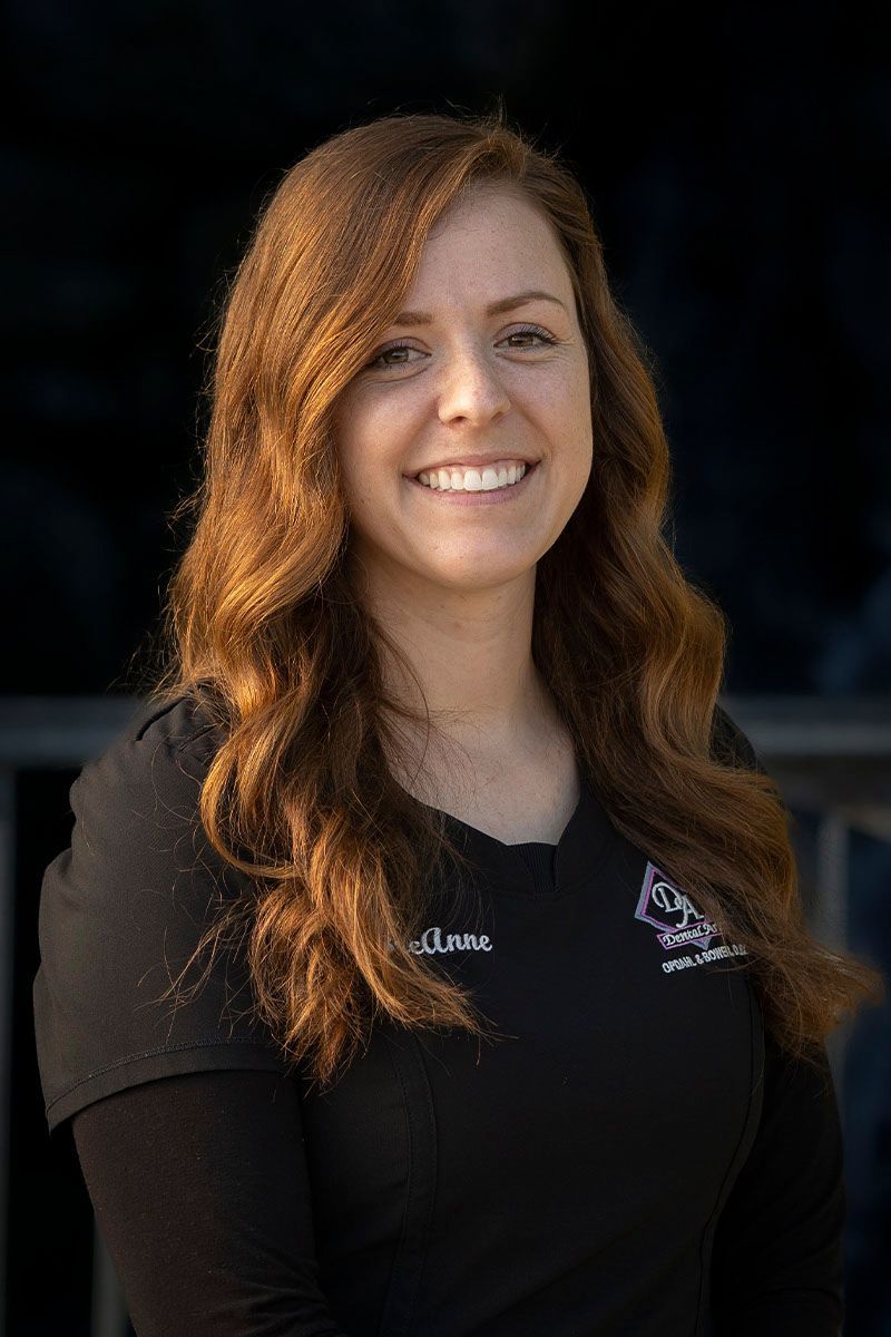A woman with long brown hair is smiling and wearing a black shirt.