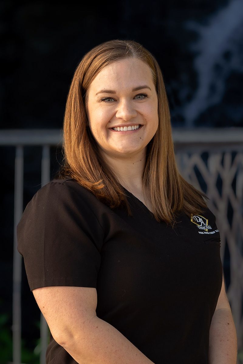 Dentist Dr. Daecy in a black scrub top is smiling and standing in front of a building.