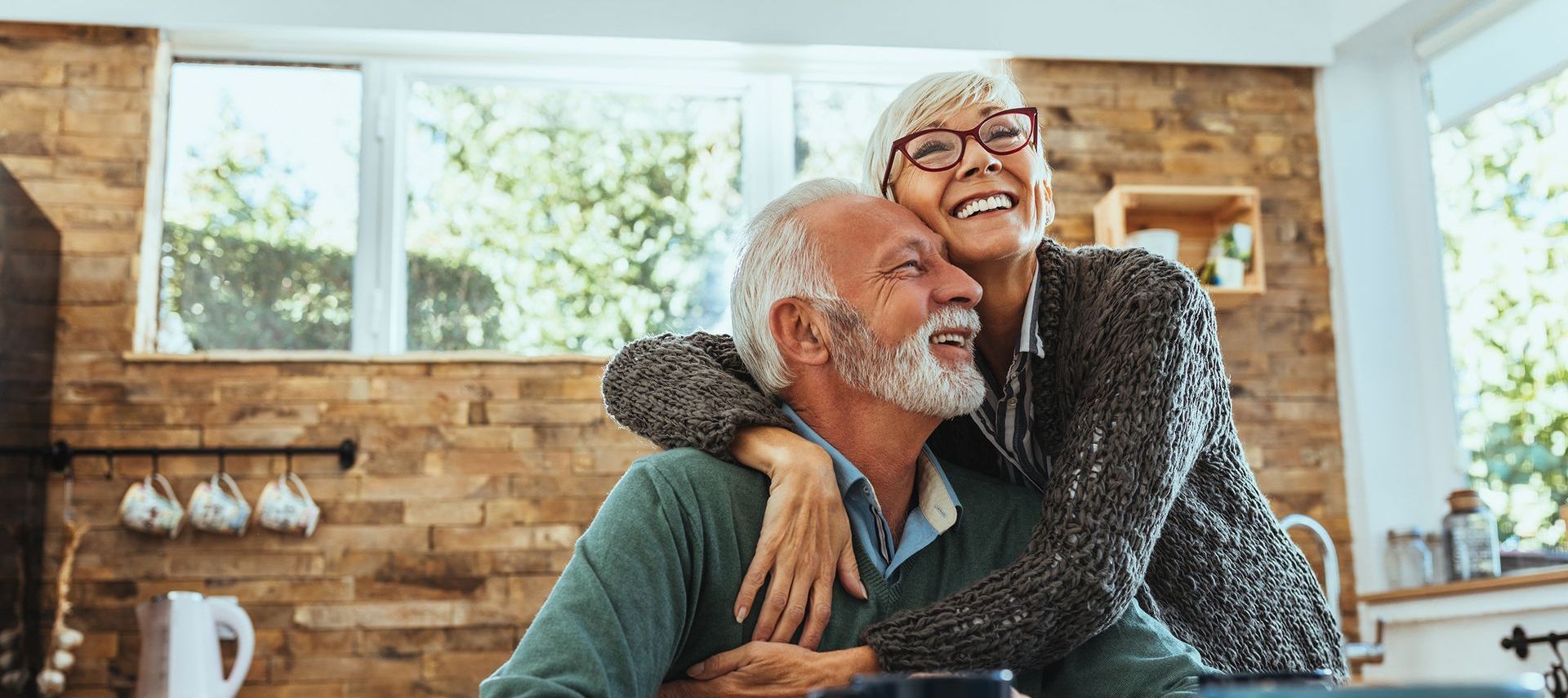 A woman is hugging an older man in a kitchen.