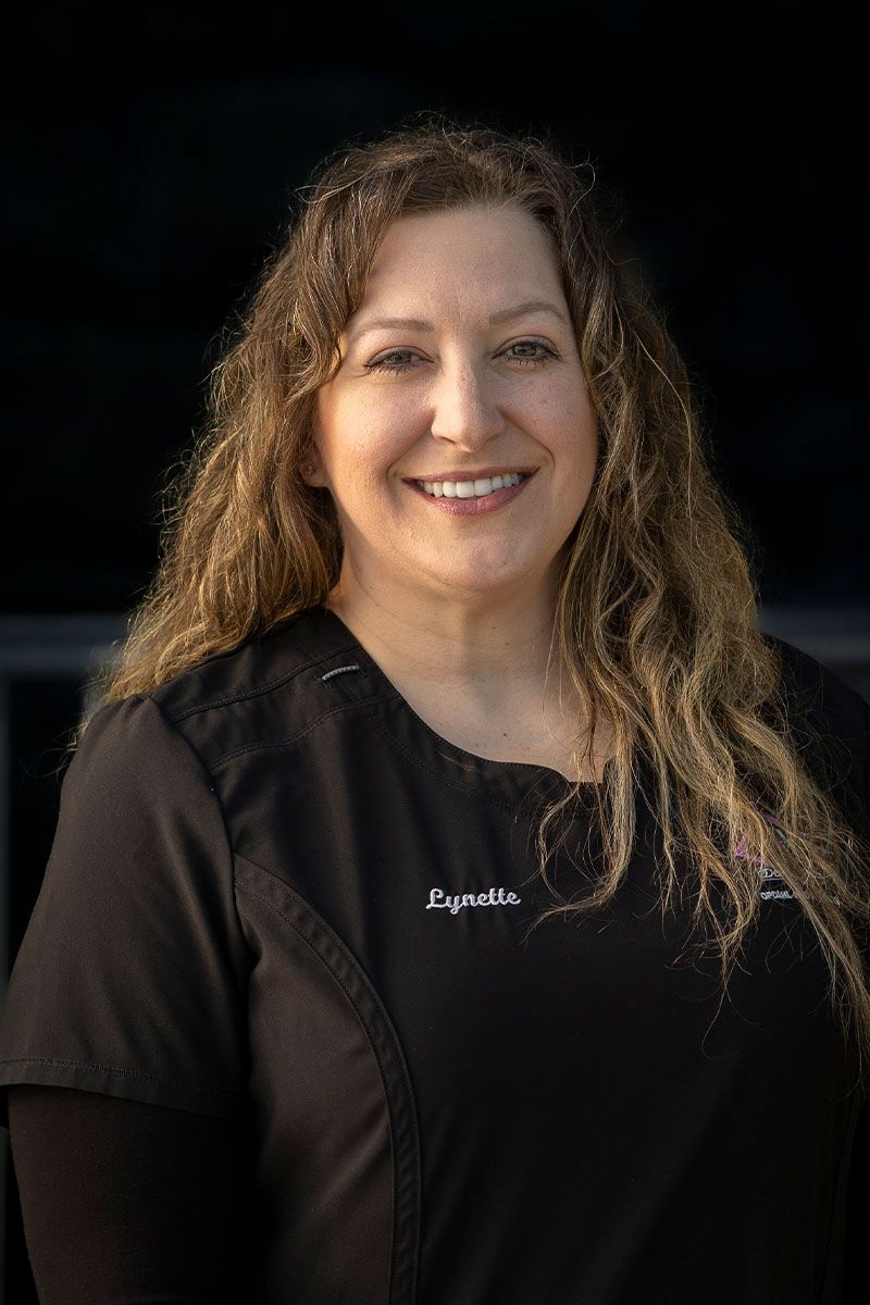 A woman in a black scrub top is smiling for the camera.