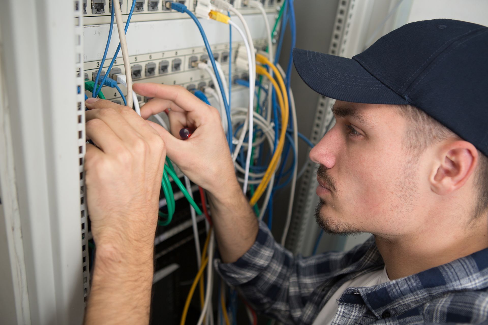 Technician working on wiring inside an electrical panel filled with colorful cables.