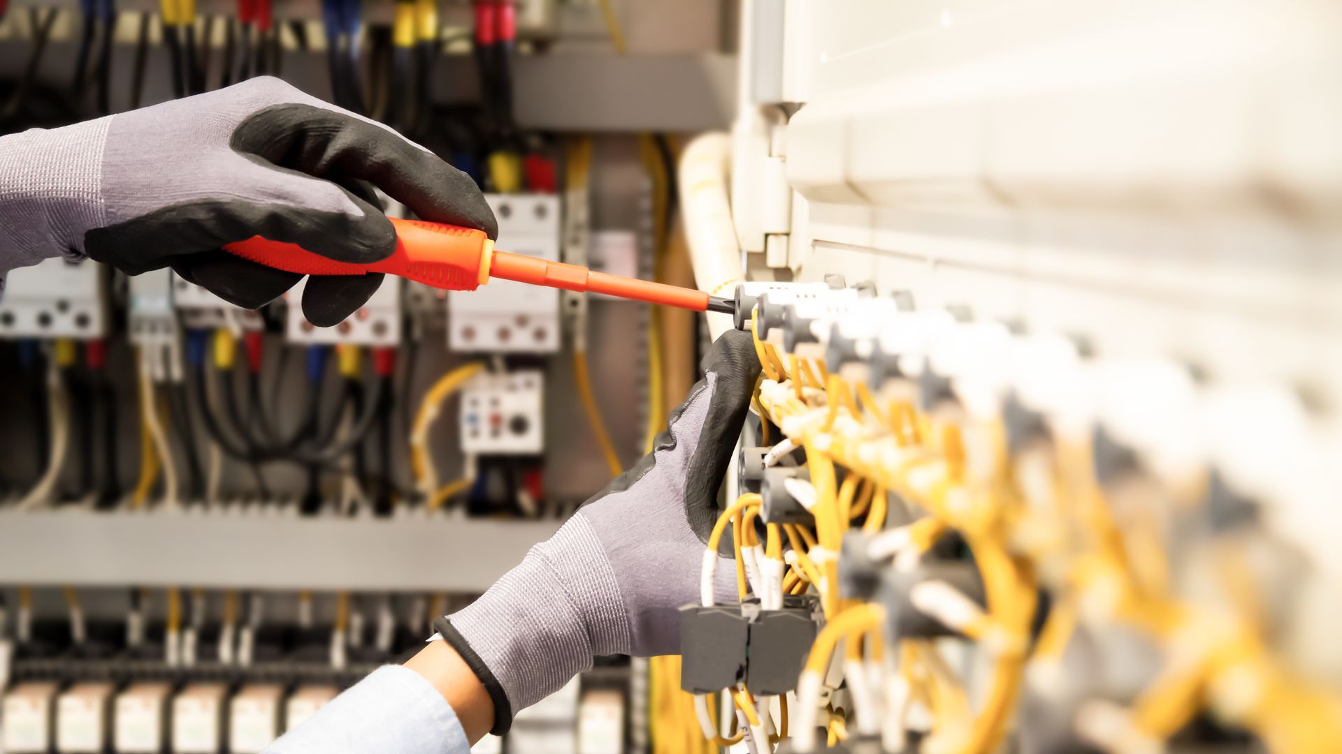 Licensed electrician repairing electrical panel using screwdriver with safety gloves on wiring.