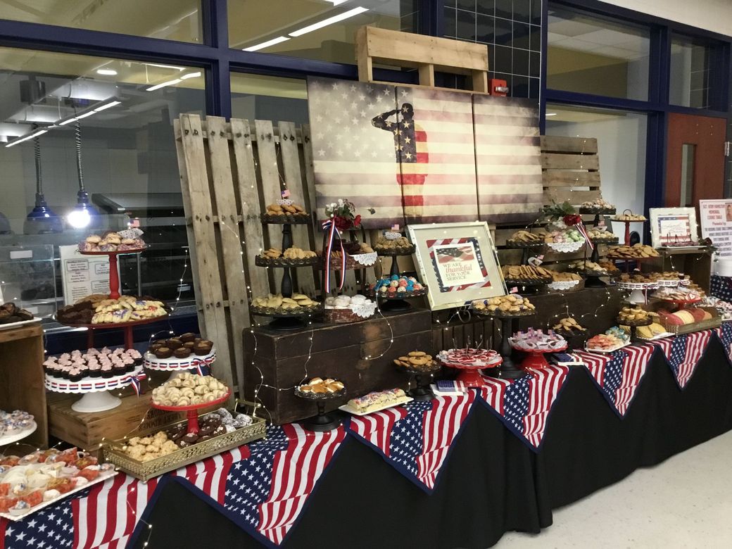 A long table decorated with American flag fabric, displaying an assortment of desserts on tiered stands and wooden crates.