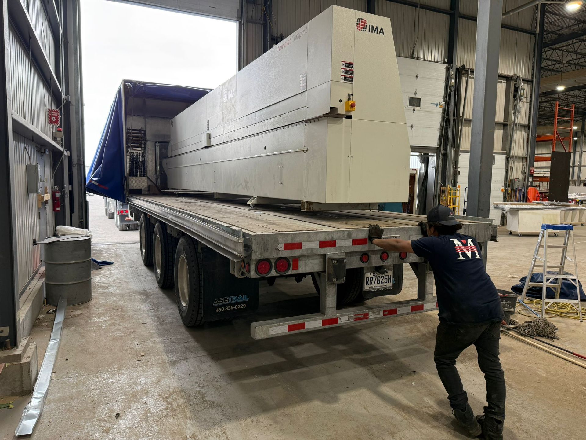 Man pushing a large white machine off a flatbed truck into a warehouse.