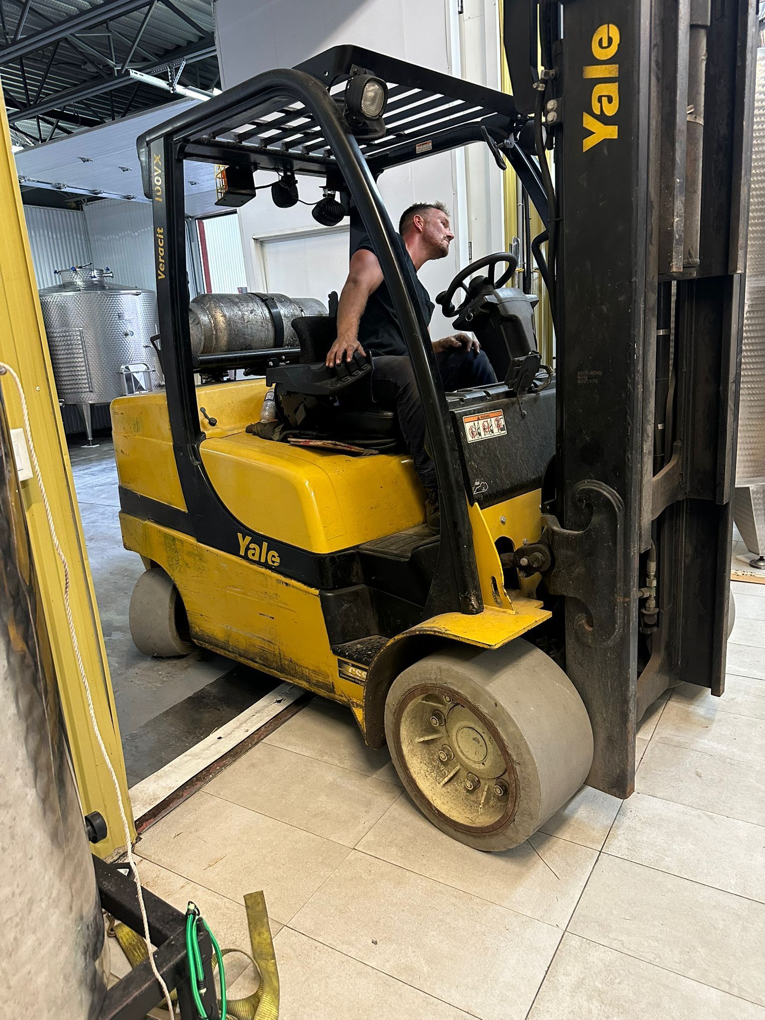 A man operates a yellow Yale forklift in a warehouse.