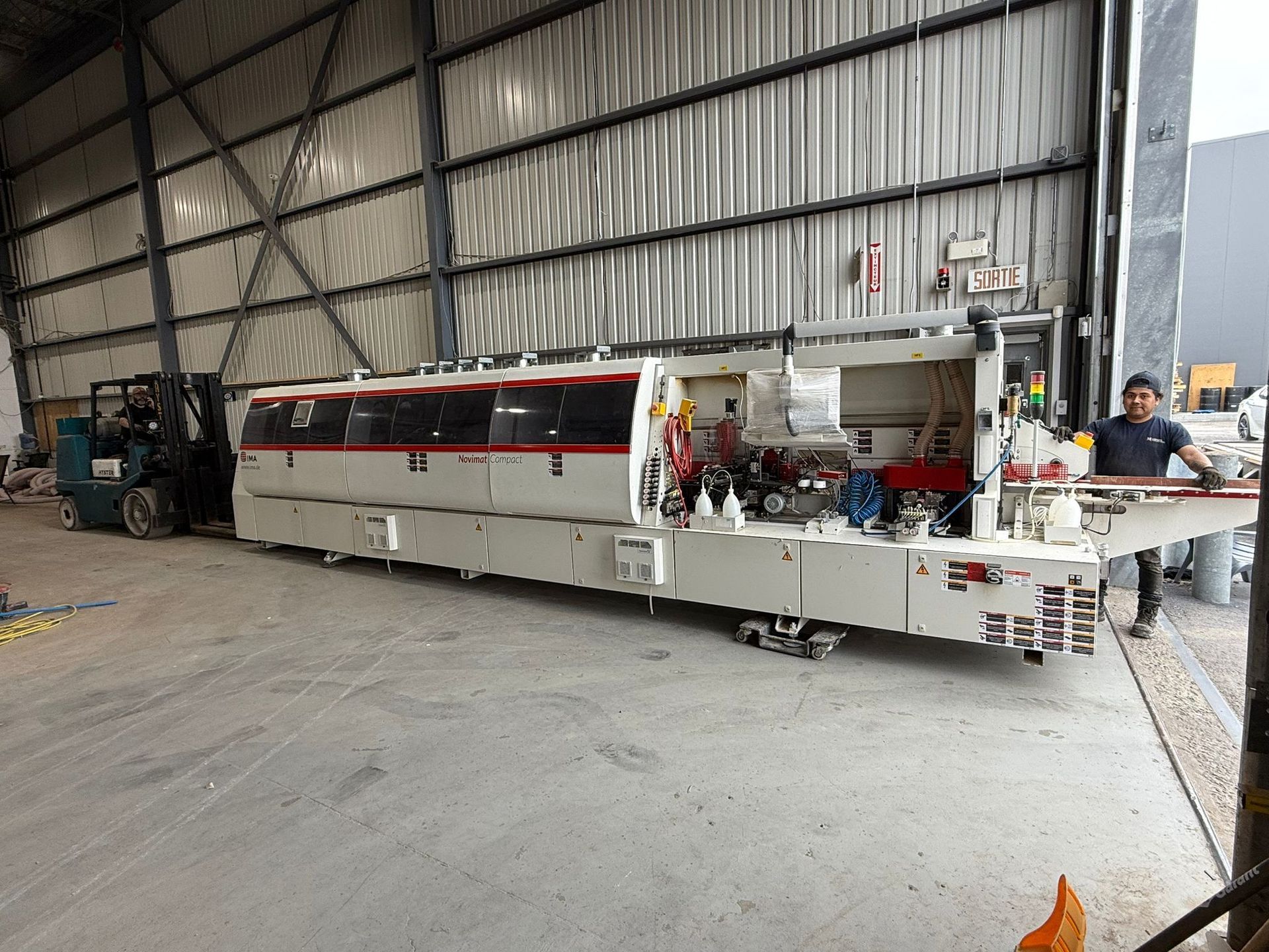 A long, white industrial machine inside a warehouse, with a person standing next to it.
