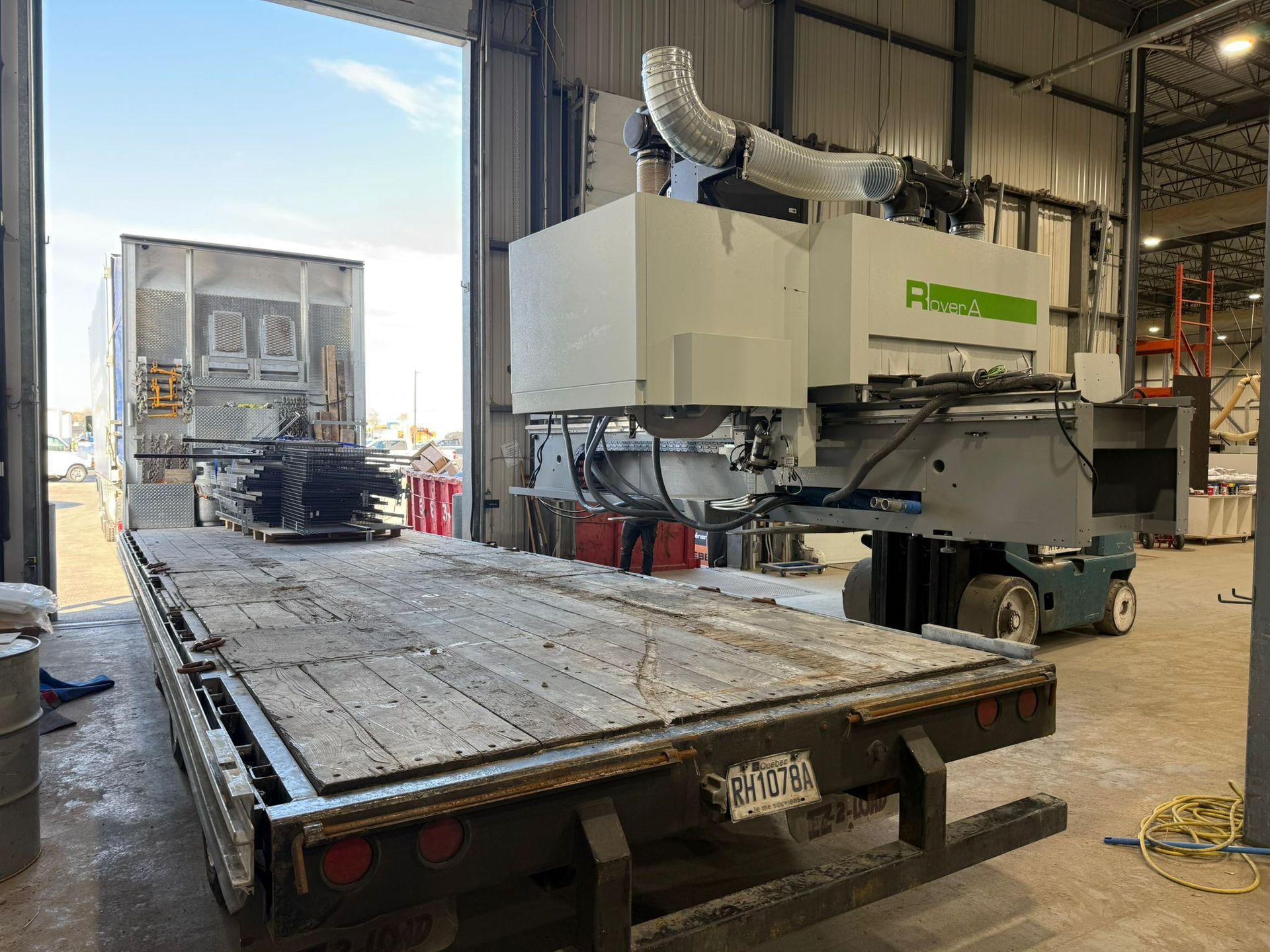 A large industrial machine is being unloaded from a flatbed trailer inside a warehouse.