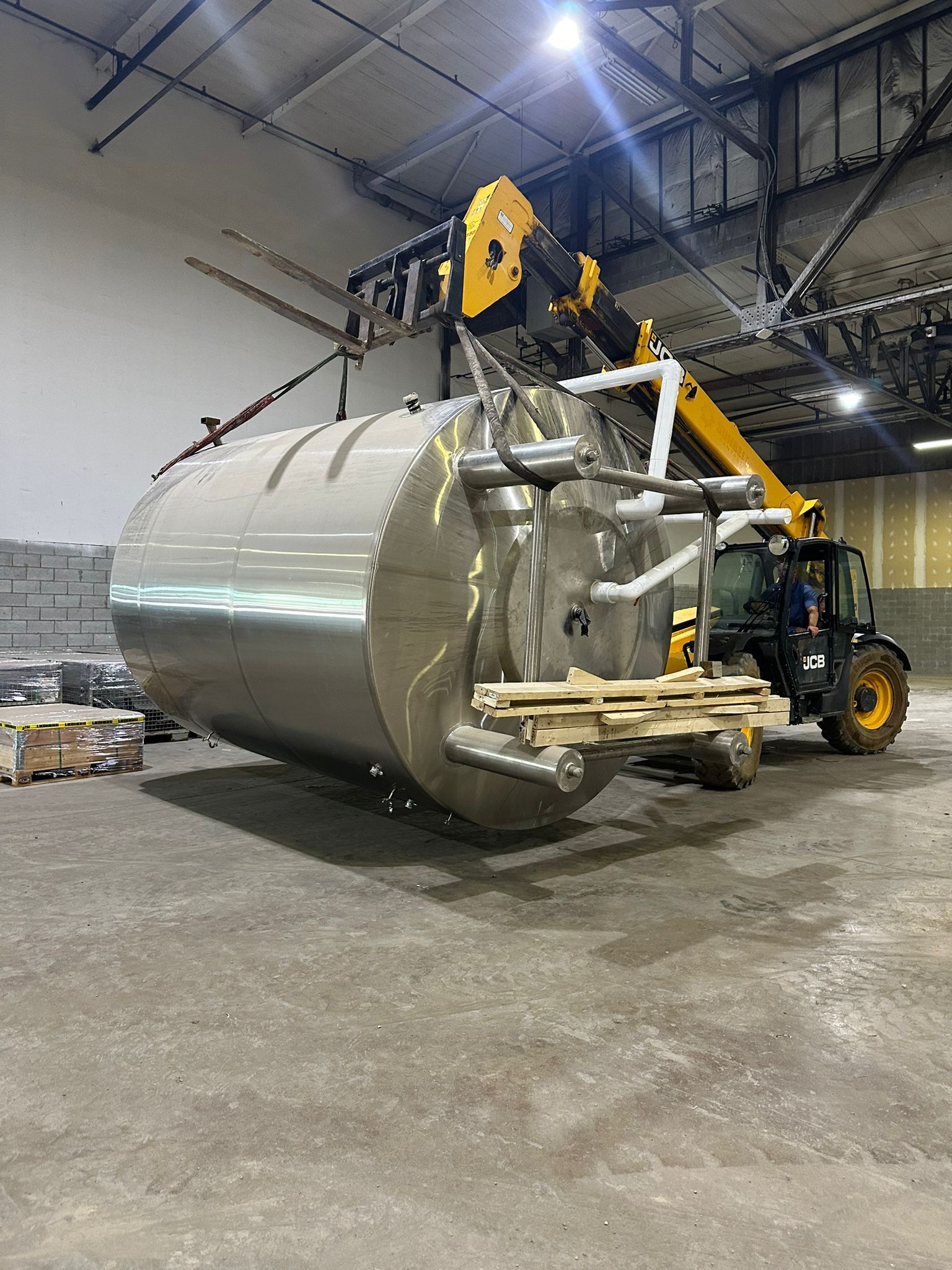 A large, shiny metal tank is lifted by a yellow forklift in a warehouse setting.