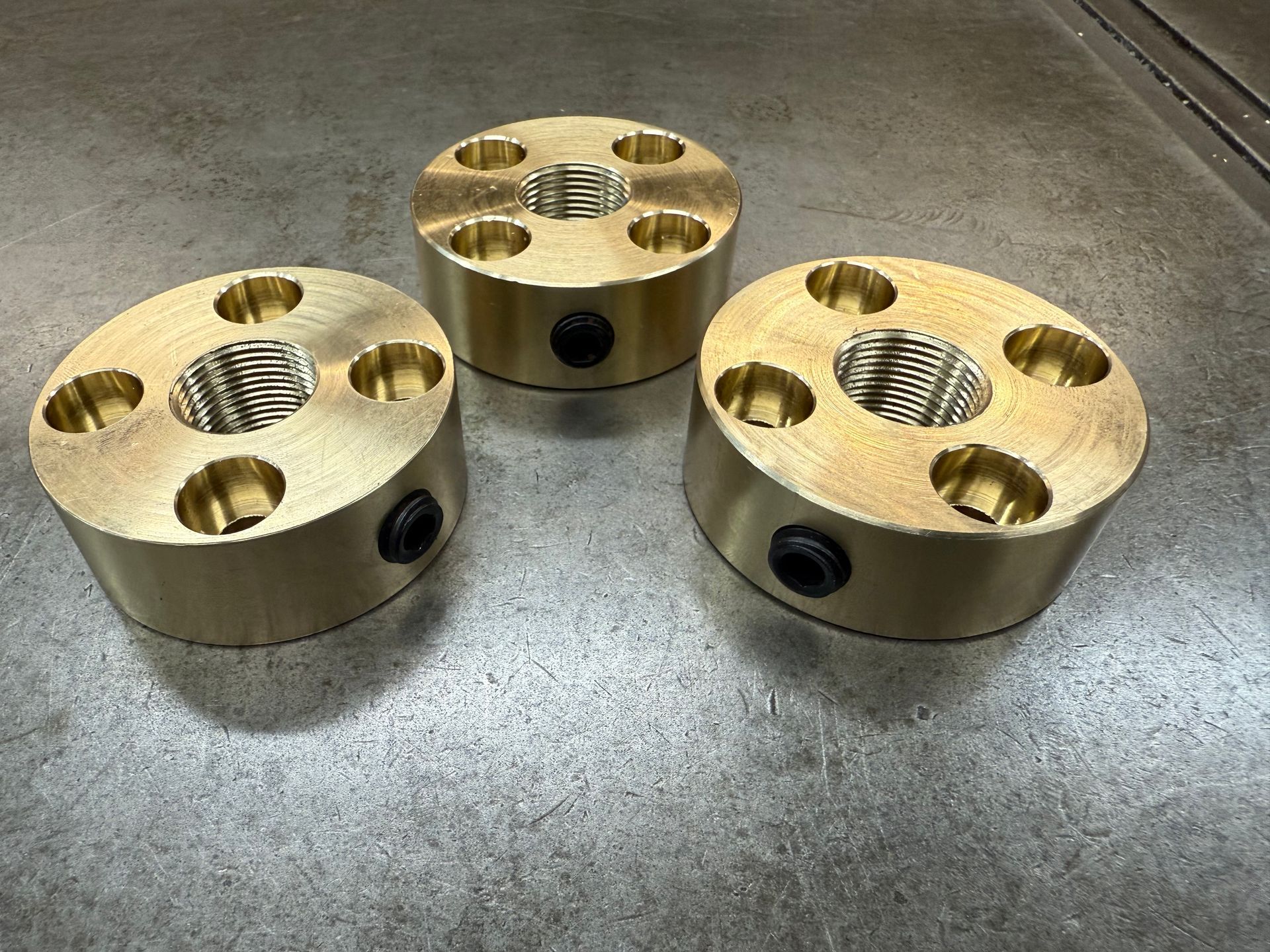 Three brass cylinders with threaded center holes and bolt holes, on a metal surface.
