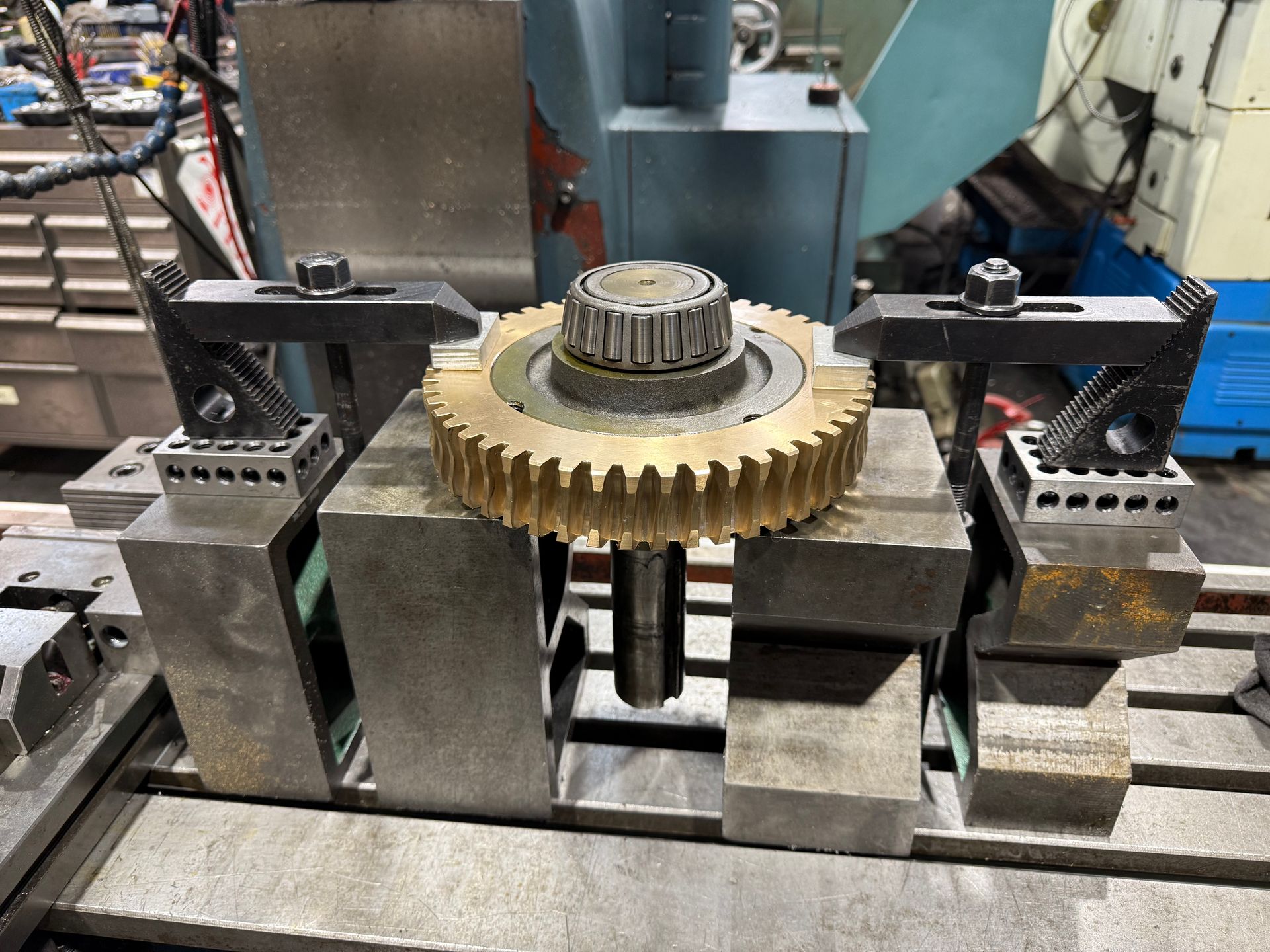 A metal gear held in place by clamps on a machine's work surface in a workshop.