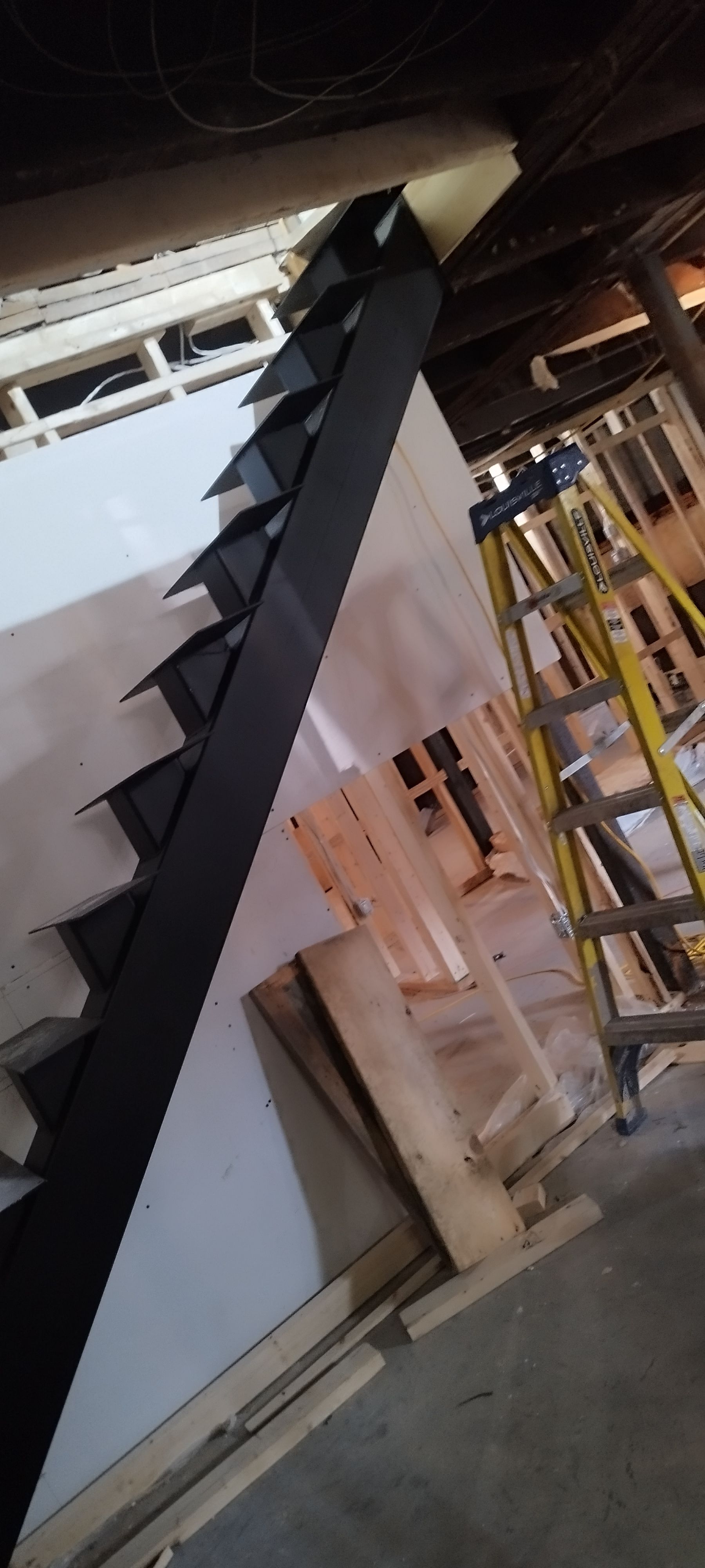 Black steel stringer stairs with white treads under construction. Yellow ladder in background.