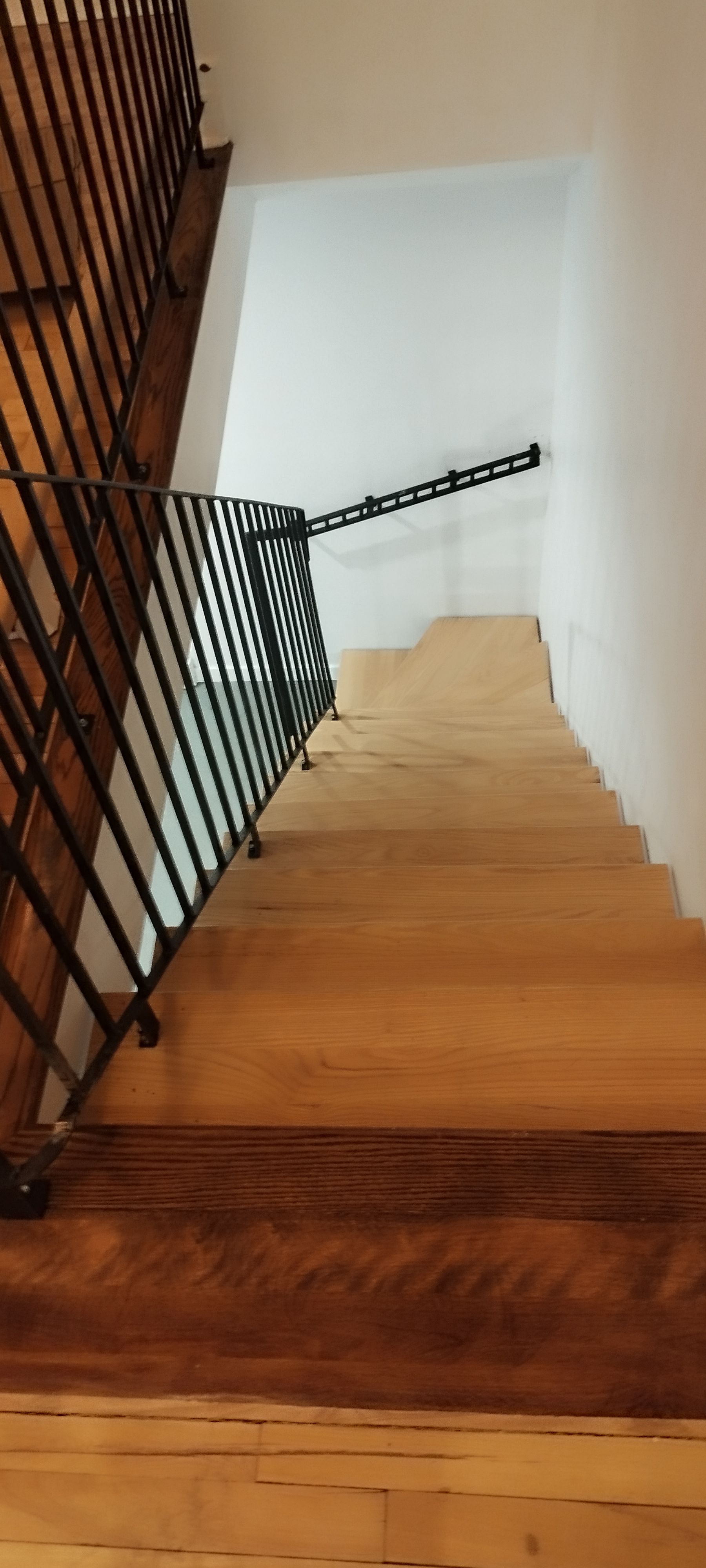 Wooden staircase with black metal railing and white walls.
