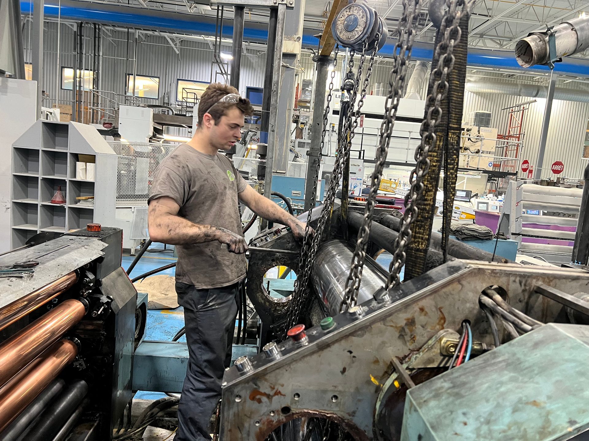 Man in a factory, working on machinery with dirty hands and clothes.
