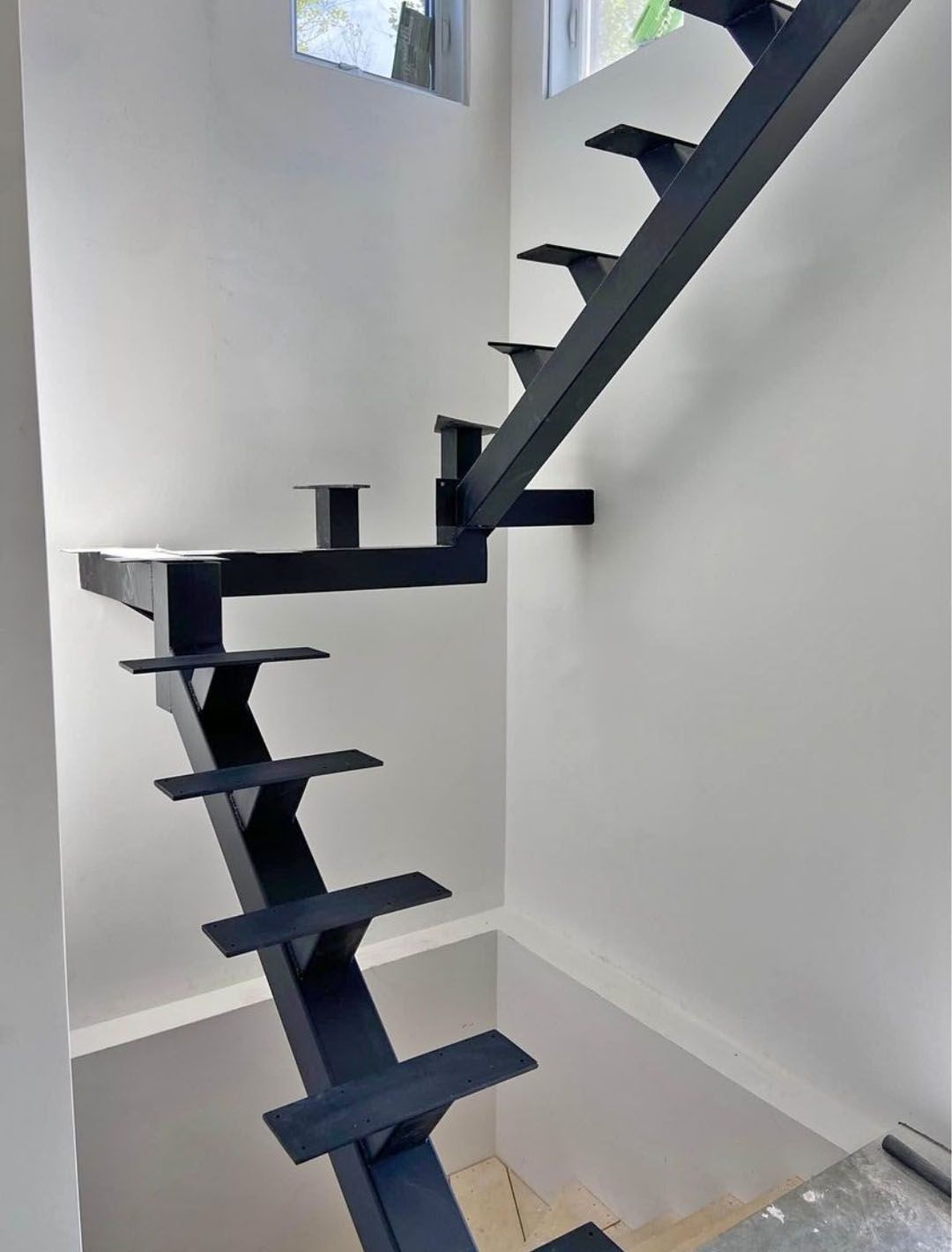 Black metal floating stairs against a white wall.
