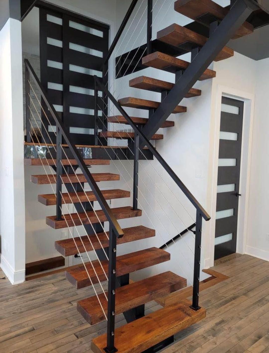 Modern wooden staircase with metal railings, leading to a dark door.