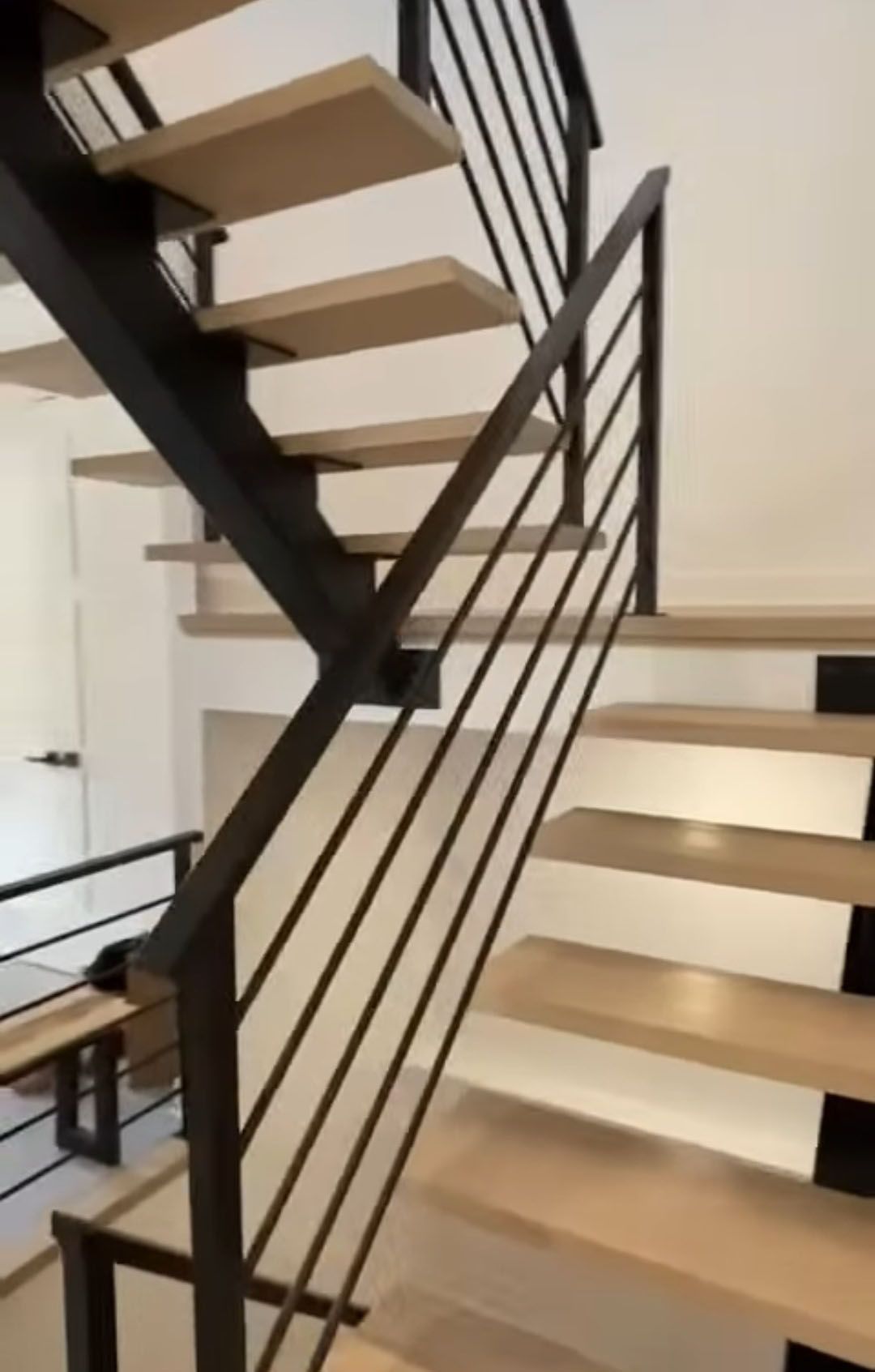 Modern staircase with light wood steps, black metal railing, and white walls.