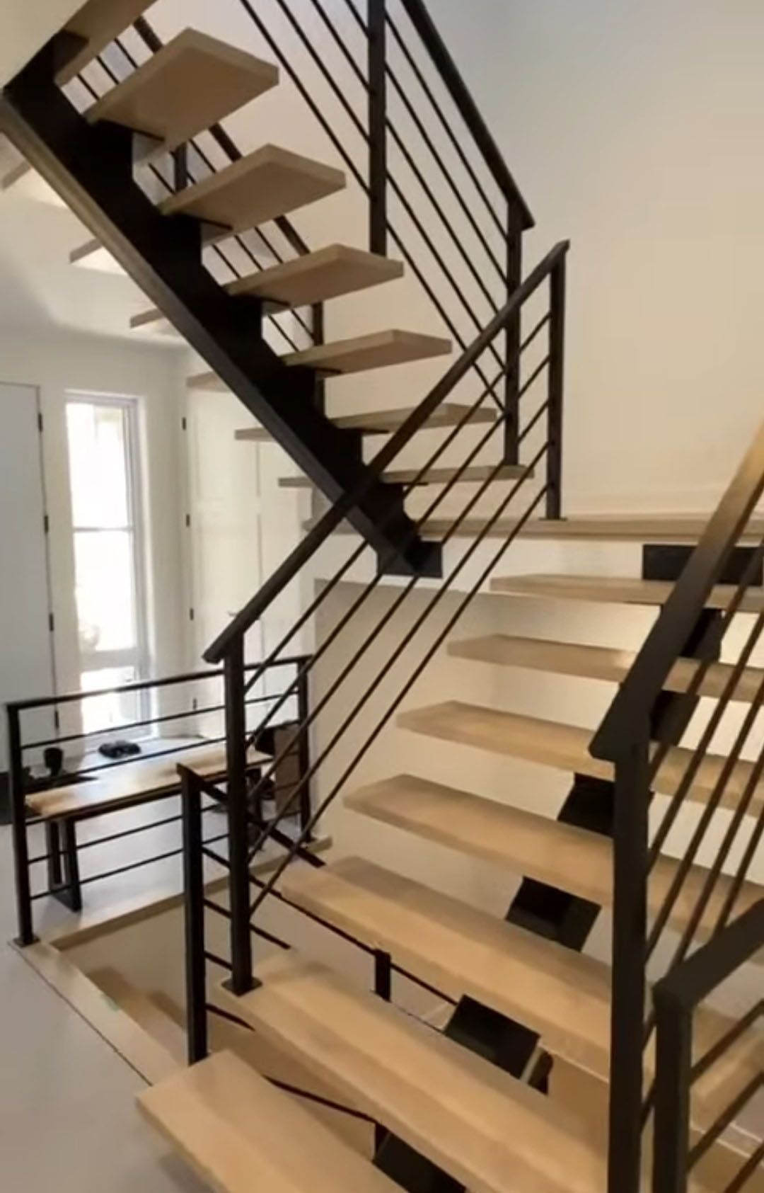 Staircase with light wood steps, black metal railing, and white walls.
