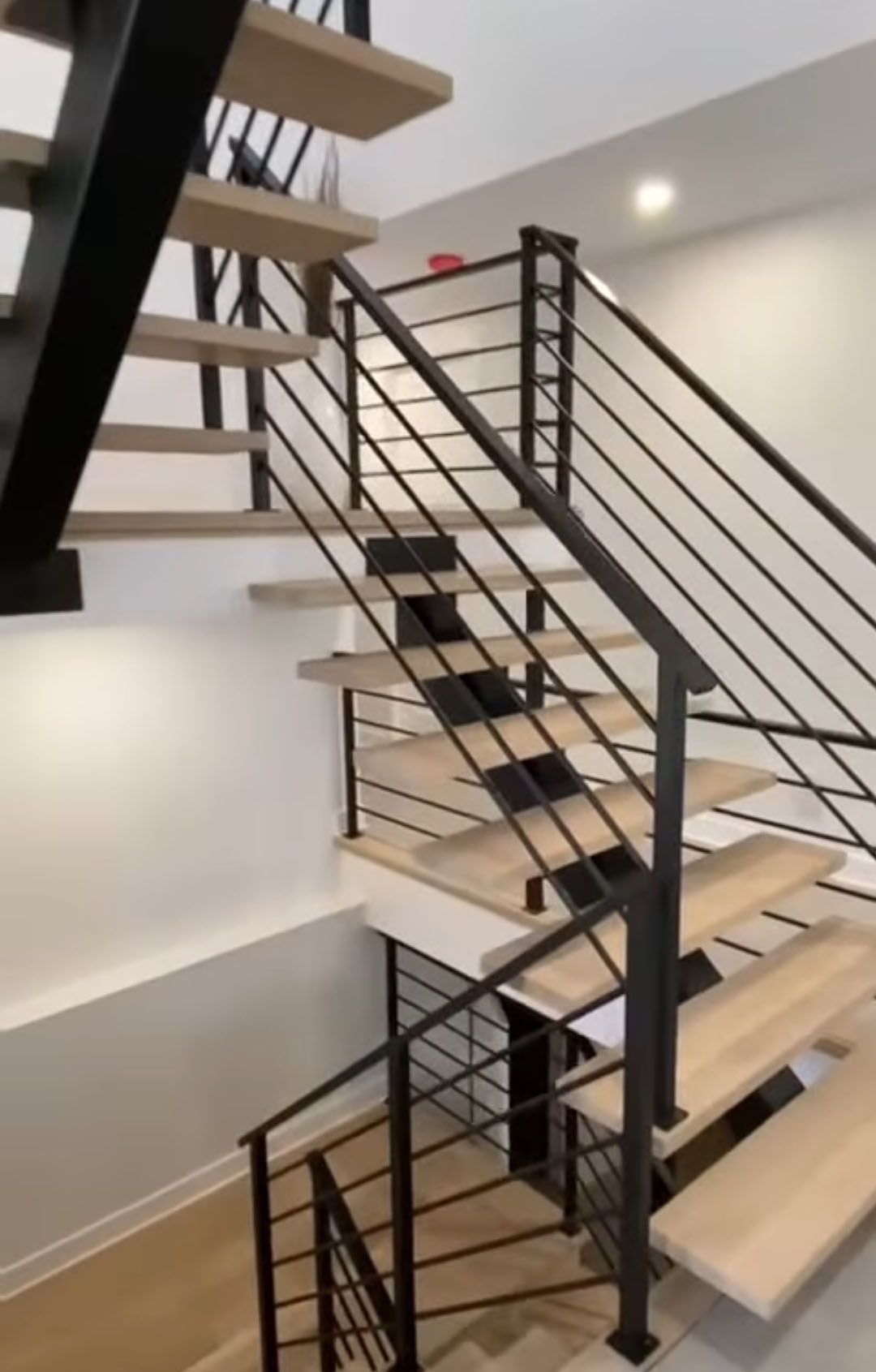 A modern staircase with light wood steps and black metal railings in a white-walled interior.