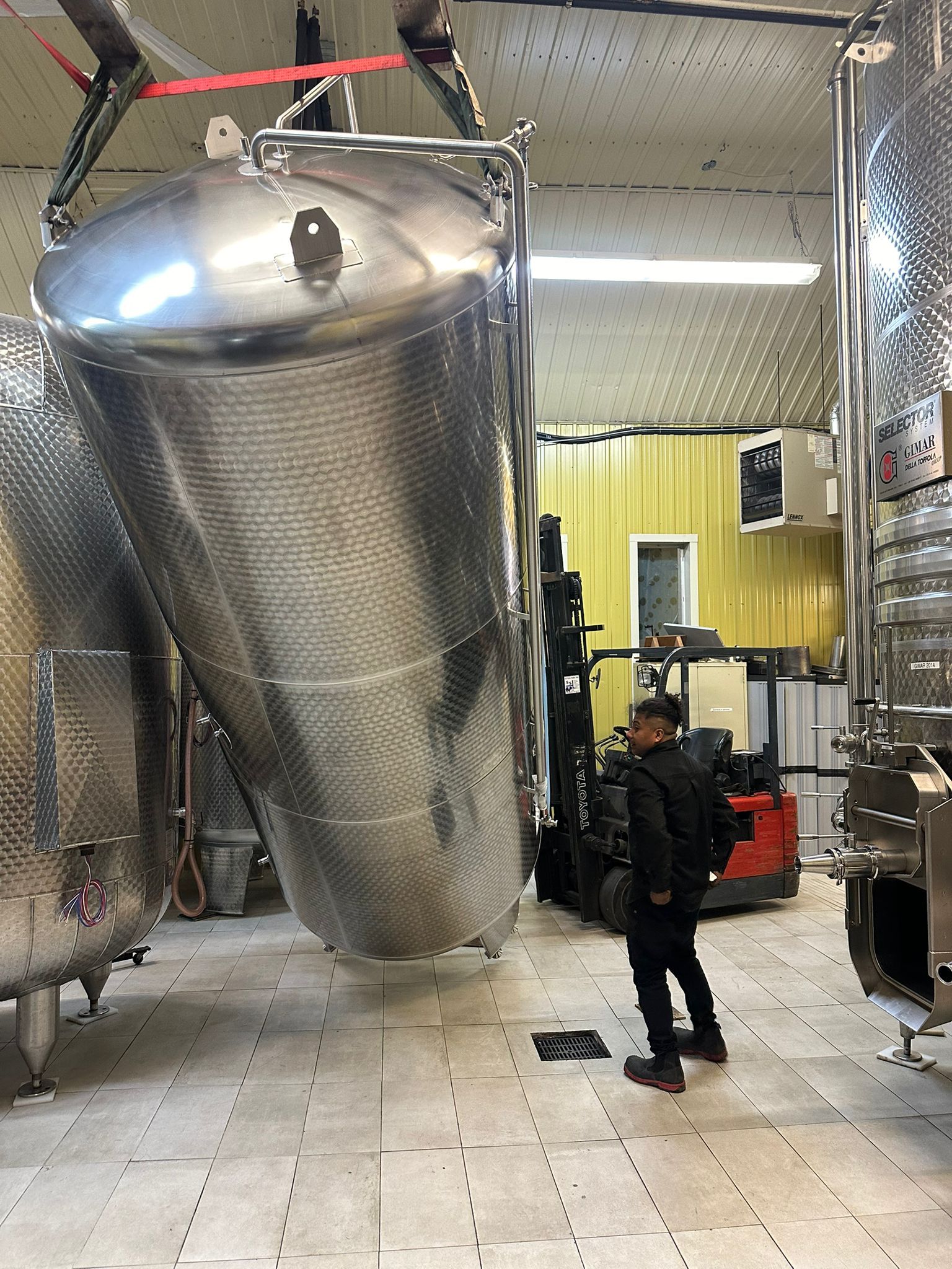 A worker watches a stainless steel tank being lifted inside a winery.