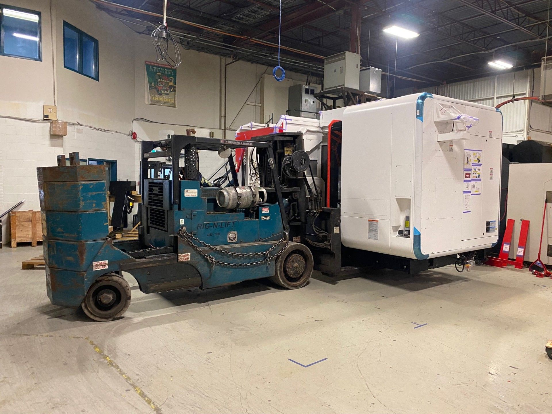 A forklift in a warehouse carrying a large white rectangular object.