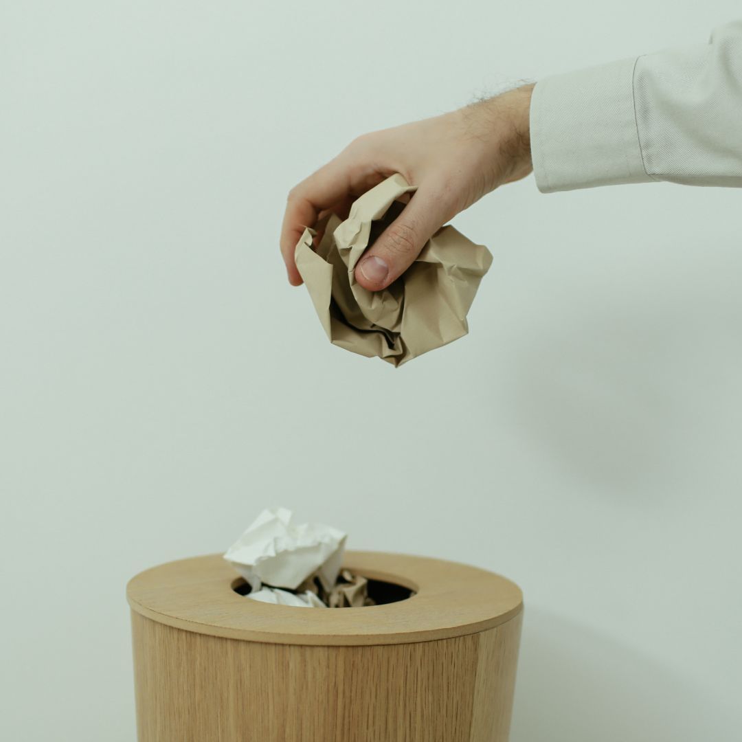 Mão jogando papel amassado no lixo, simbolizando decisões de carreira feitas sem direção.