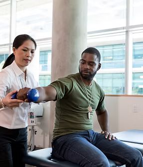 Physical therapist helping a patient exercise his arm with a blue dumbbell in a bright clinic.