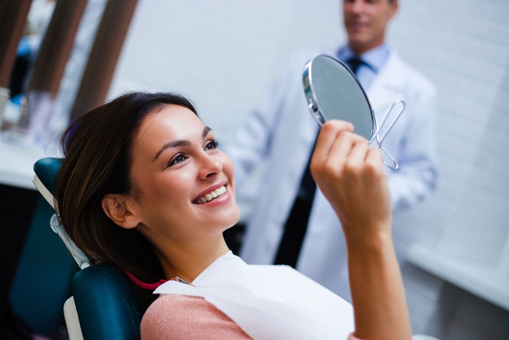 A Person Sitting in a Dental Chair Smiles While Holding a Hand Mirror to Inspect Their Teeth — Smiles on Hudson In Hamilton, NSW
