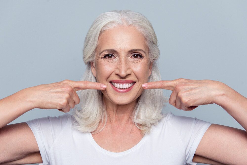 Woman With Gray Hair Smiles, Pointing at Her Bright White Teeth — Smiles on Hudson In Port Stephens, NSW