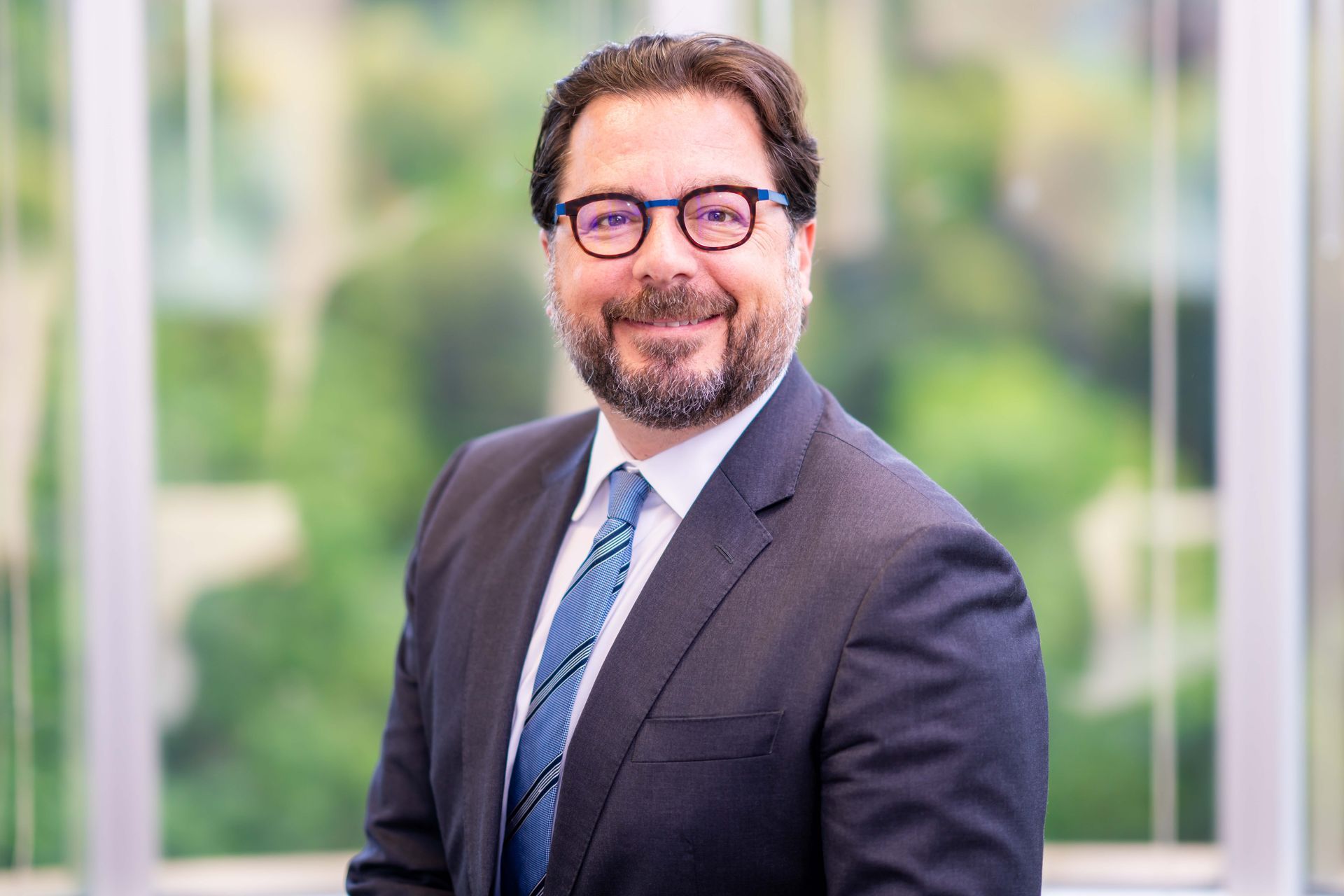A man in a suit and tie is smiling in front of a window.