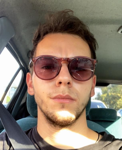 Man wearing sunglasses in a car, looking forward.