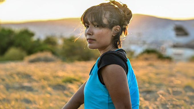 Woman in blue shirt looks over shoulder at sunset in field.
