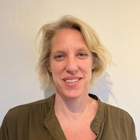 Woman with blonde hair, wearing a green shirt, smiling, in front of a white background.