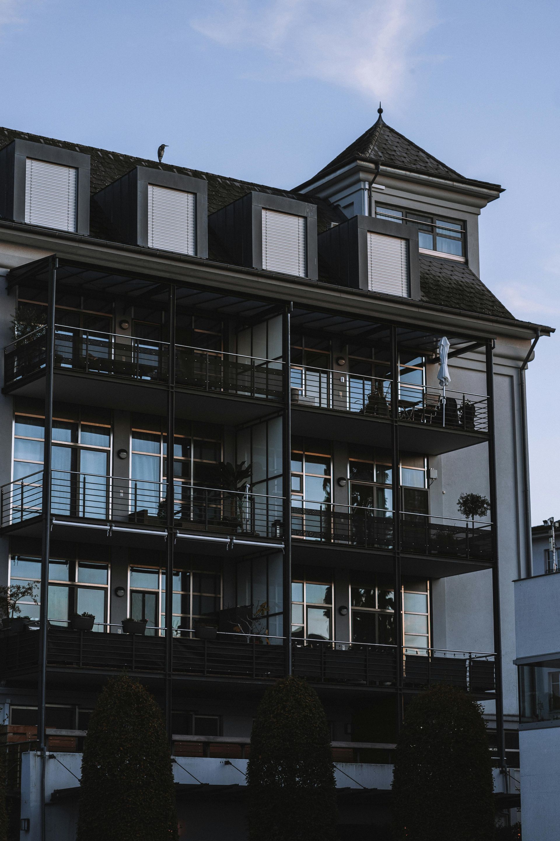Multi-story apartment building with balconies and a turret against a blue sky.