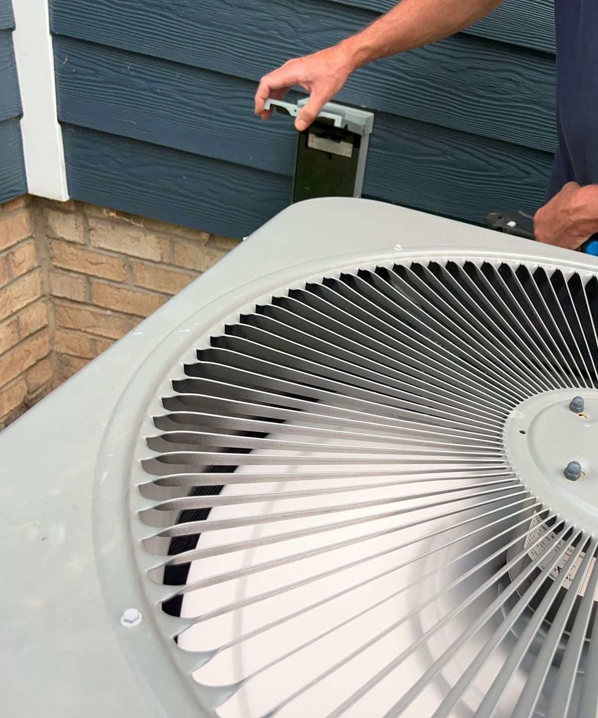 A man is working on an air conditioner outside of a house.