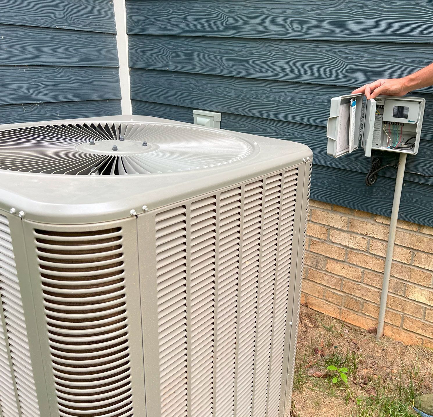 A person is working on an air conditioner outside of a house.