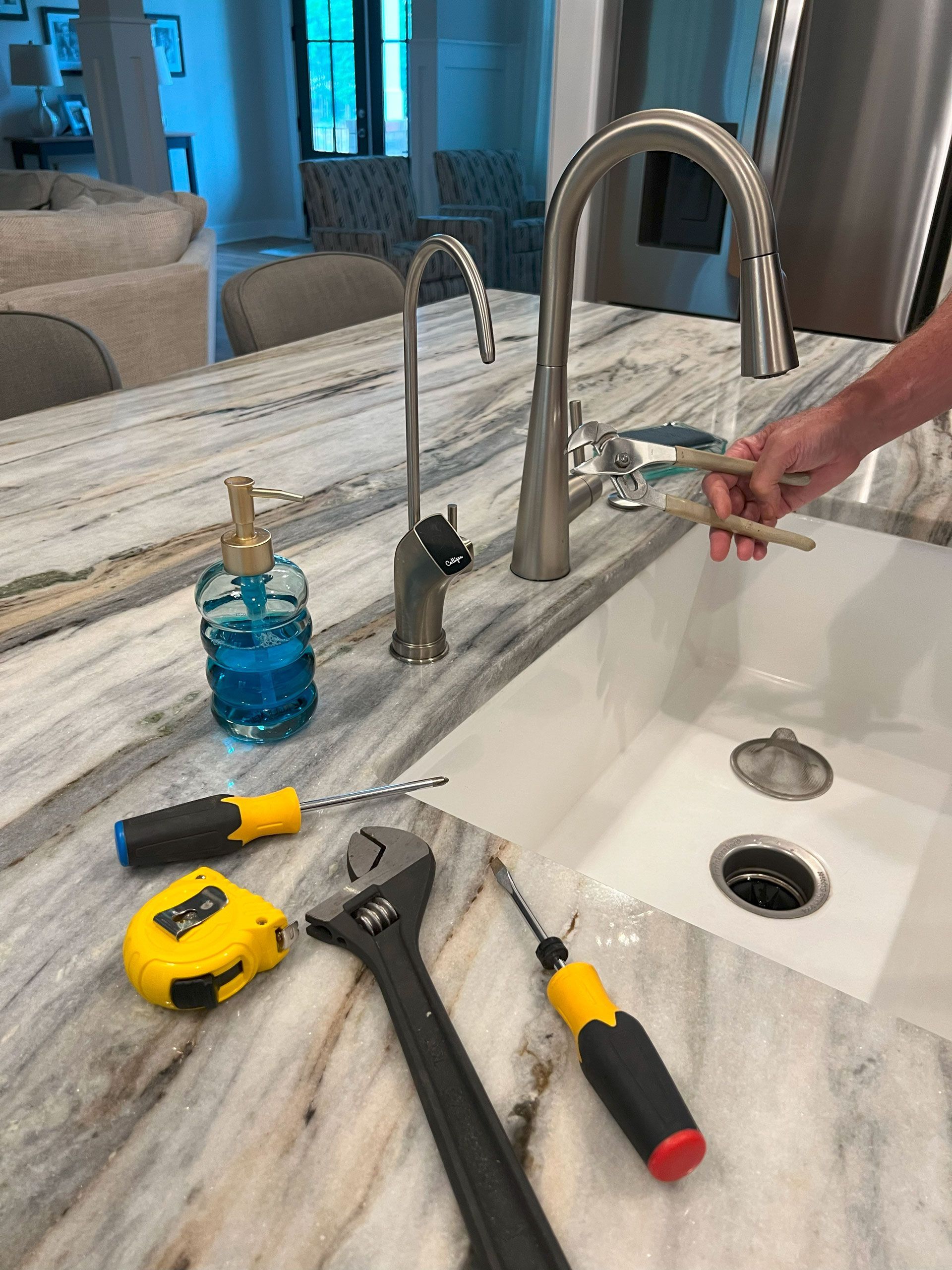 A person is fixing a kitchen sink with tools on the counter.