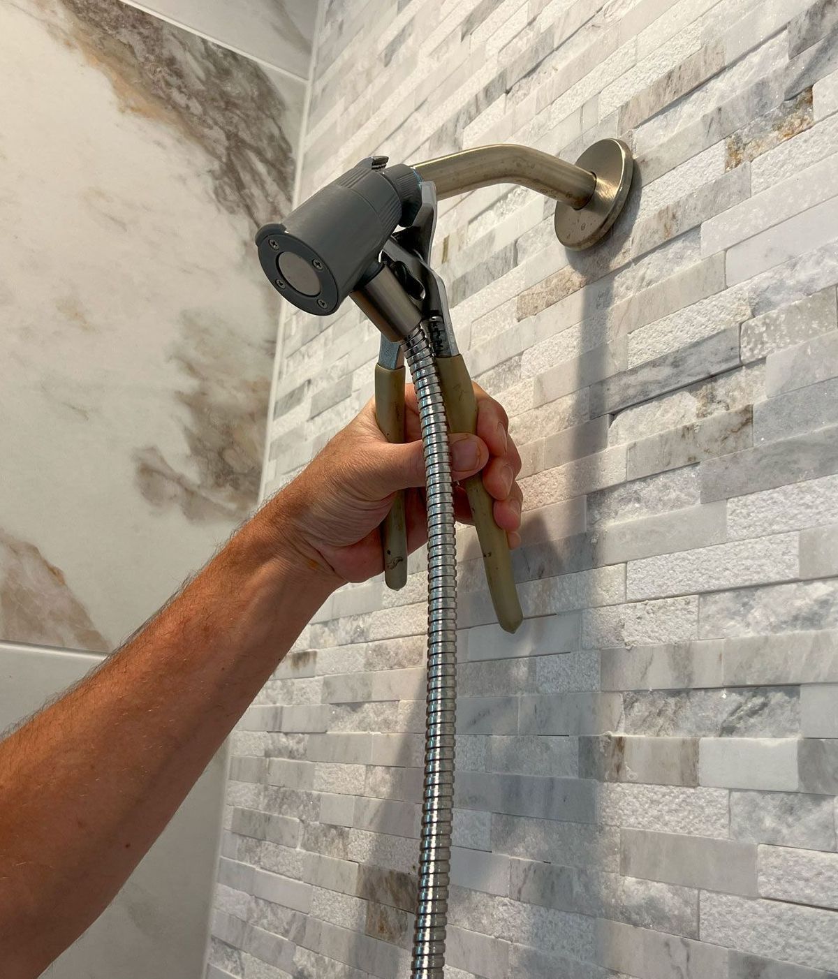 A person is fixing a shower head with a pair of pliers.