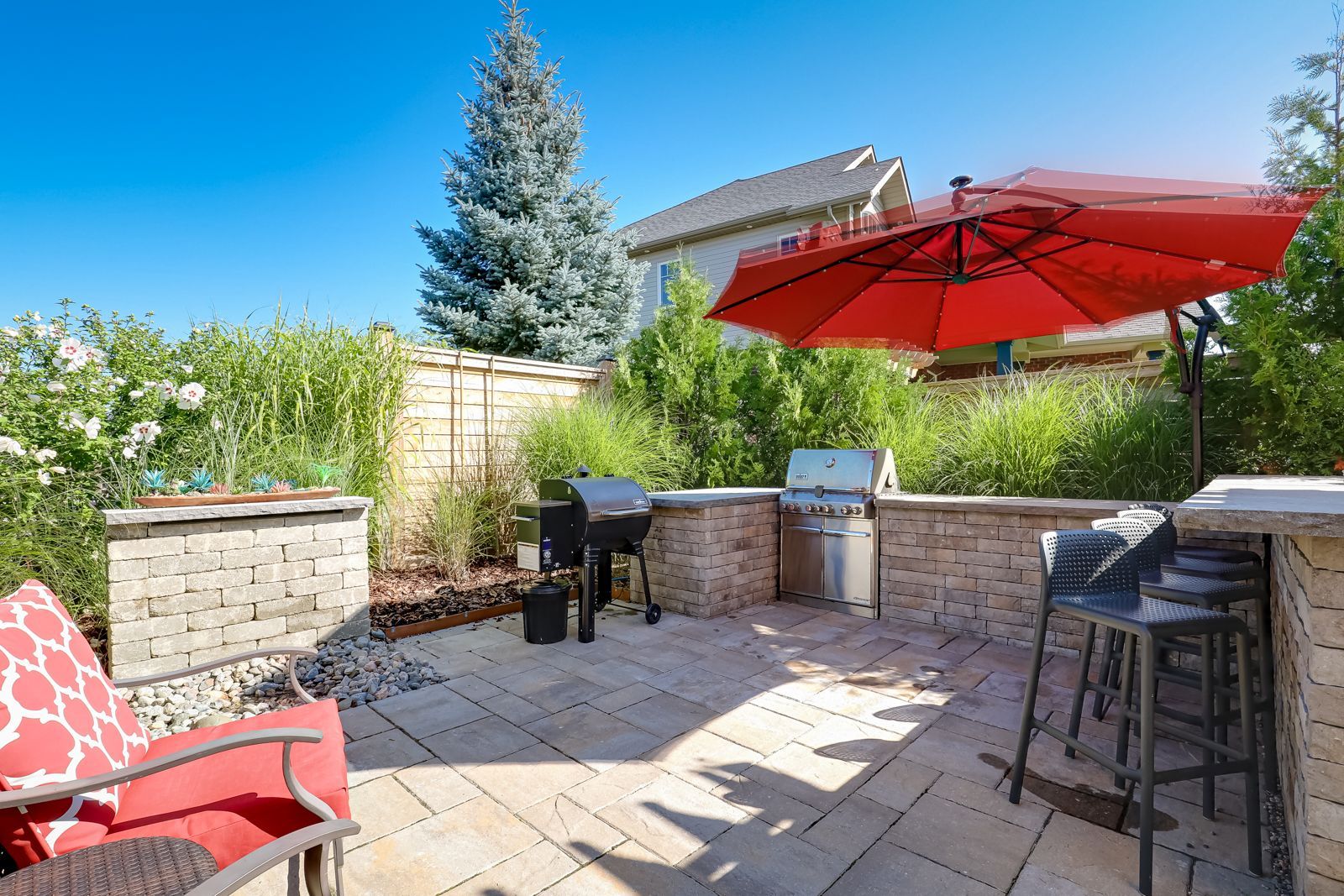 A patio with a red umbrella and a grill.