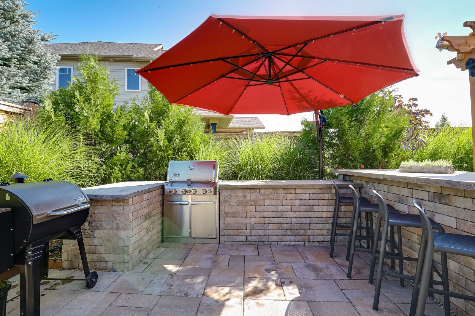 A red umbrella is sitting on top of a patio next to a grill.