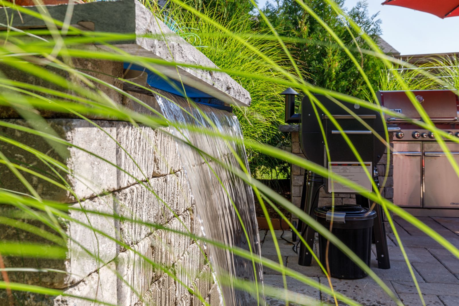 A waterfall is surrounded by tall grass and a grill.