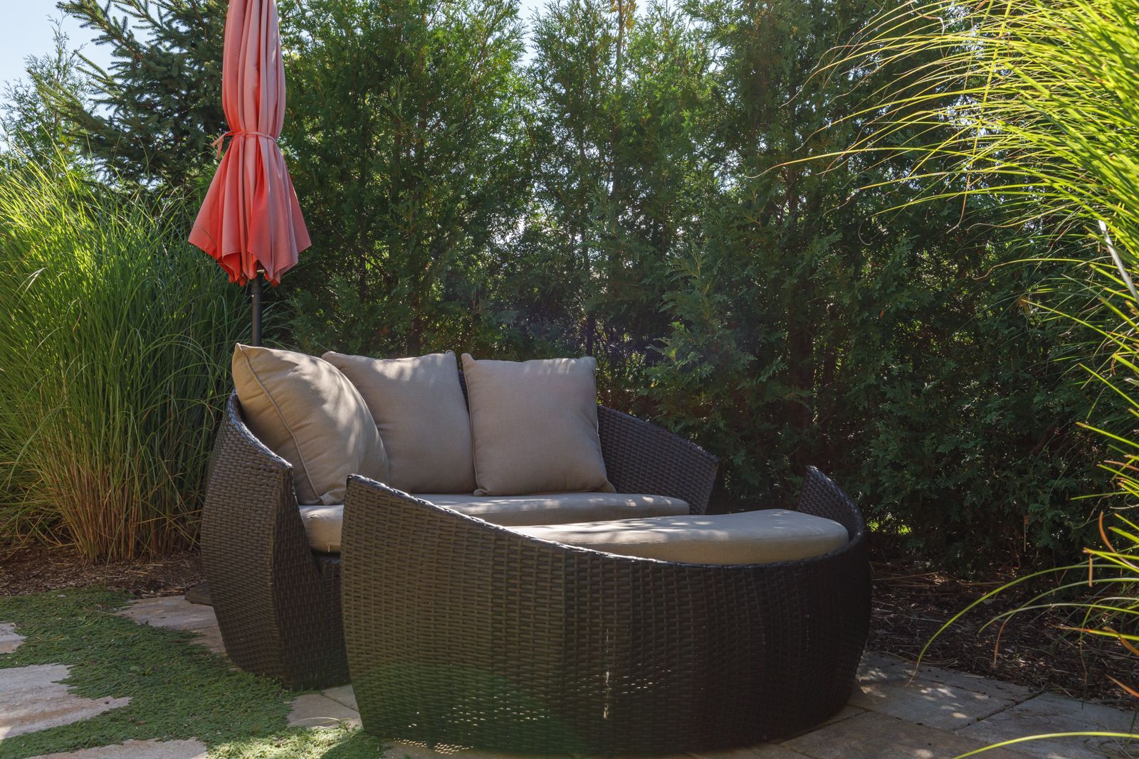 A wicker couch with a red umbrella in the background