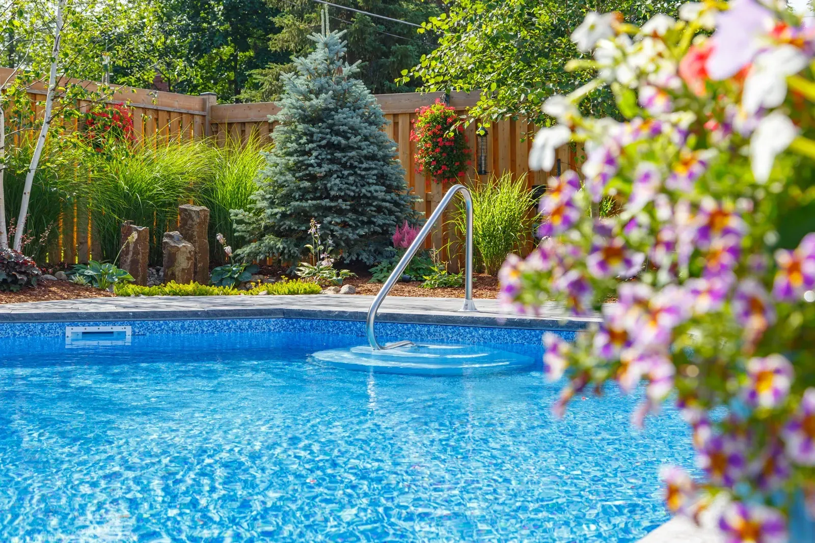 A swimming pool surrounded by flowers and trees in a backyard.