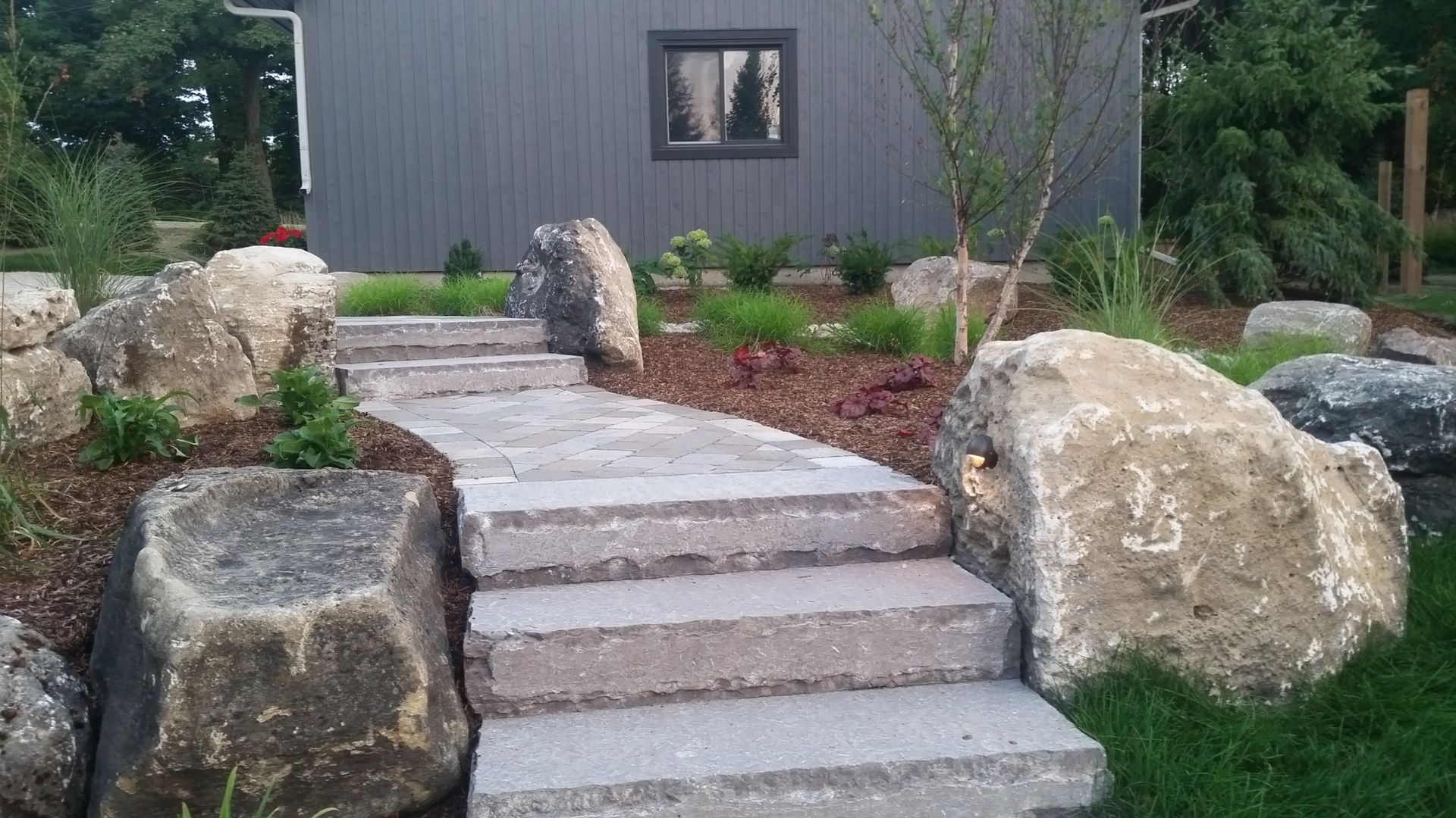 A stone walkway with steps leading up to a house surrounded by rocks.